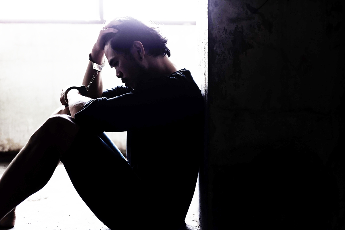 Man sitting against wall looking dejected.